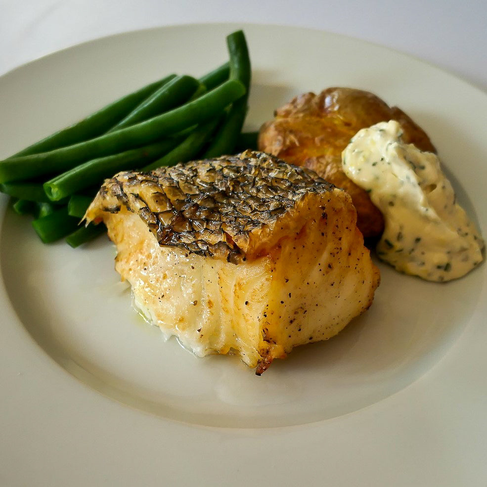 air fried piece of Chilean sea bass with green beans, roasted potatoes, and rosemary lemon aioli on a white plate