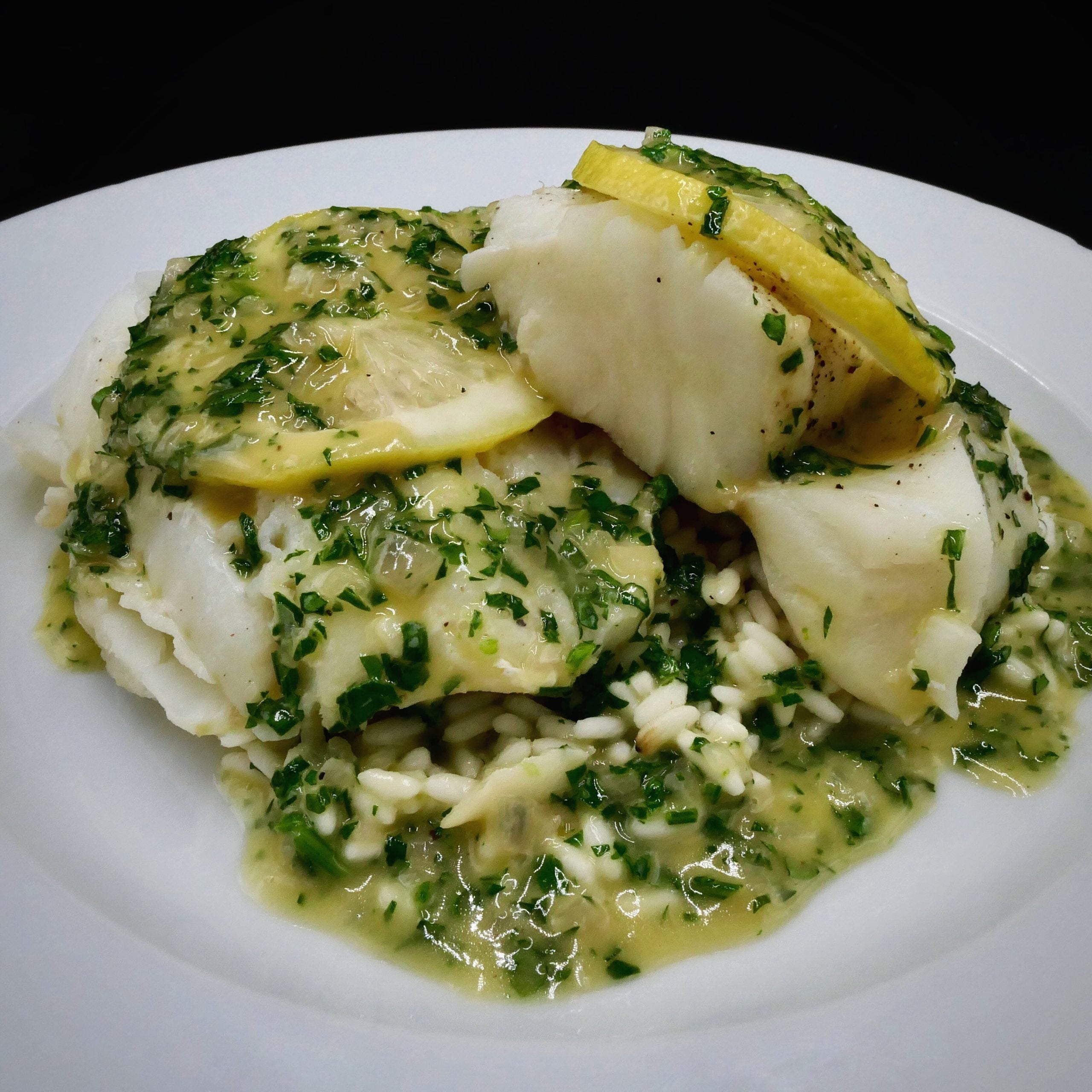 Baked Cod topped with butter, lemon, and parsley on a white plate
