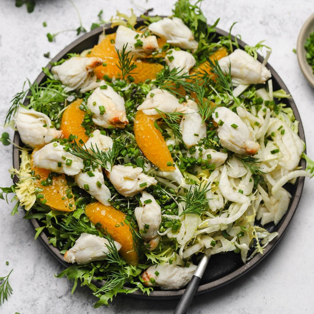 crab meat salad with citrus and fennel on black plate with white background