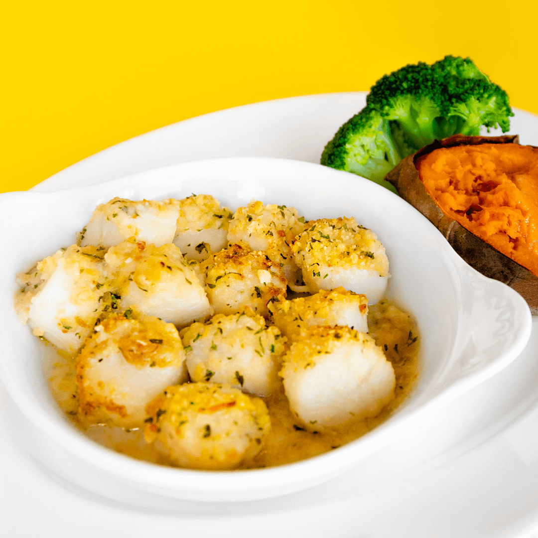 golden brown baked scallop casserole served with lemon slice and parsley on a white plate with black background