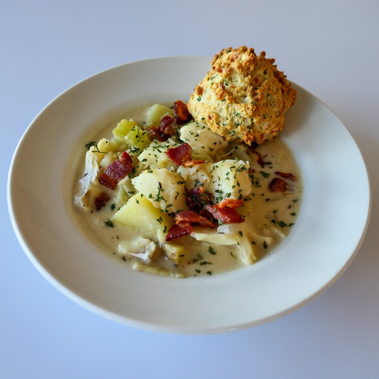 bowl of fish chowder topped with crispy bacon bits and parsley with a buttermilk biscuit on the side