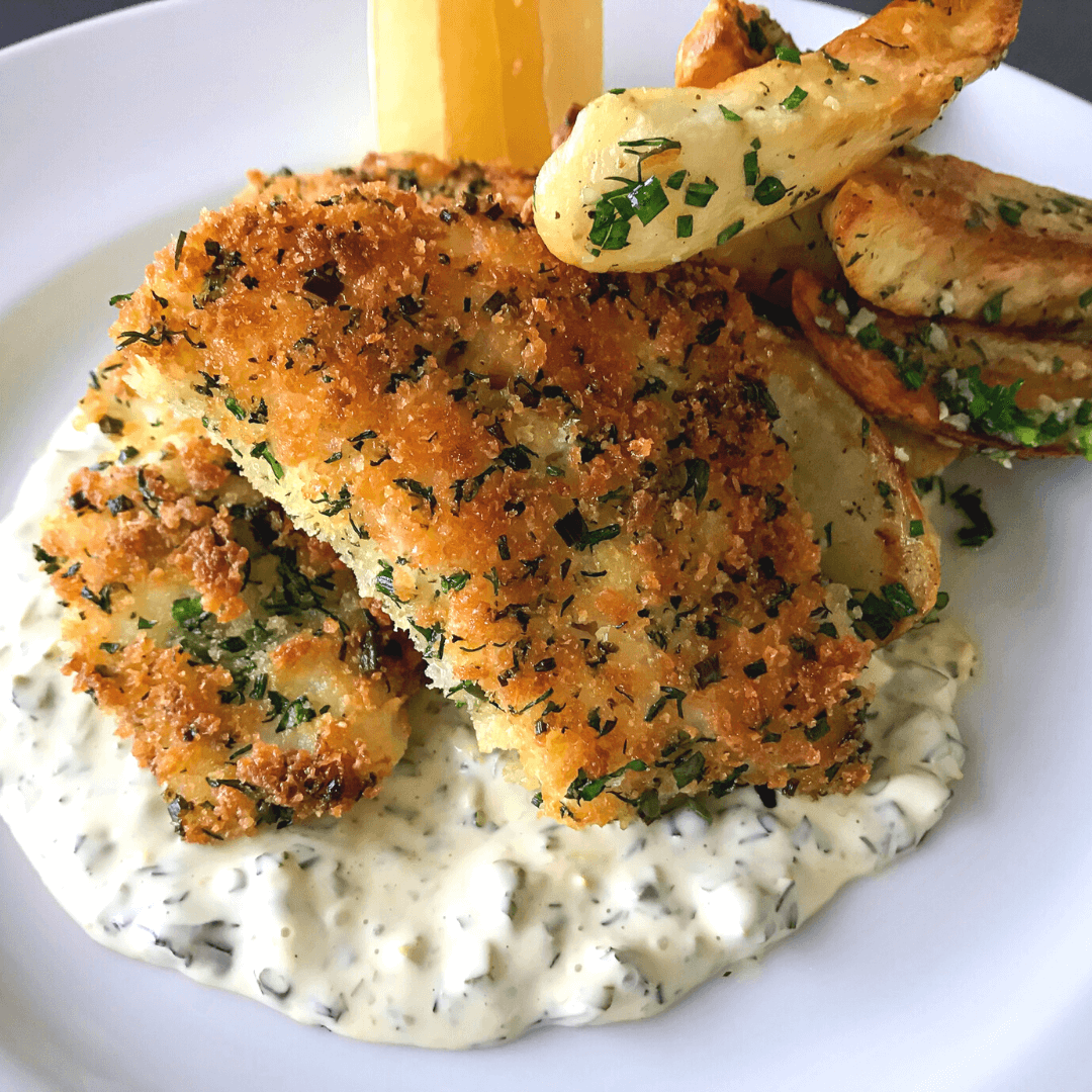 pan fried haddock with tartar sauce, fries, and lemon on a white plate