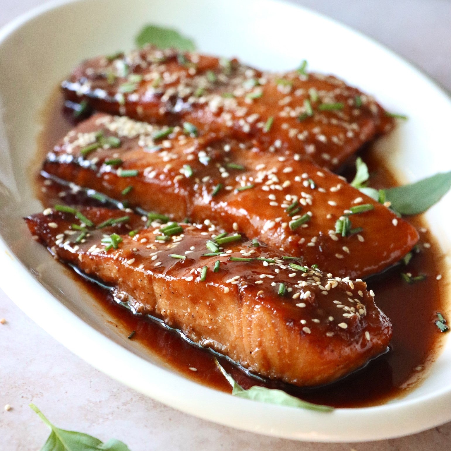 three 5 ounce portions of maple glazed salmon topped with chives and sesame seeds on a white serving plate