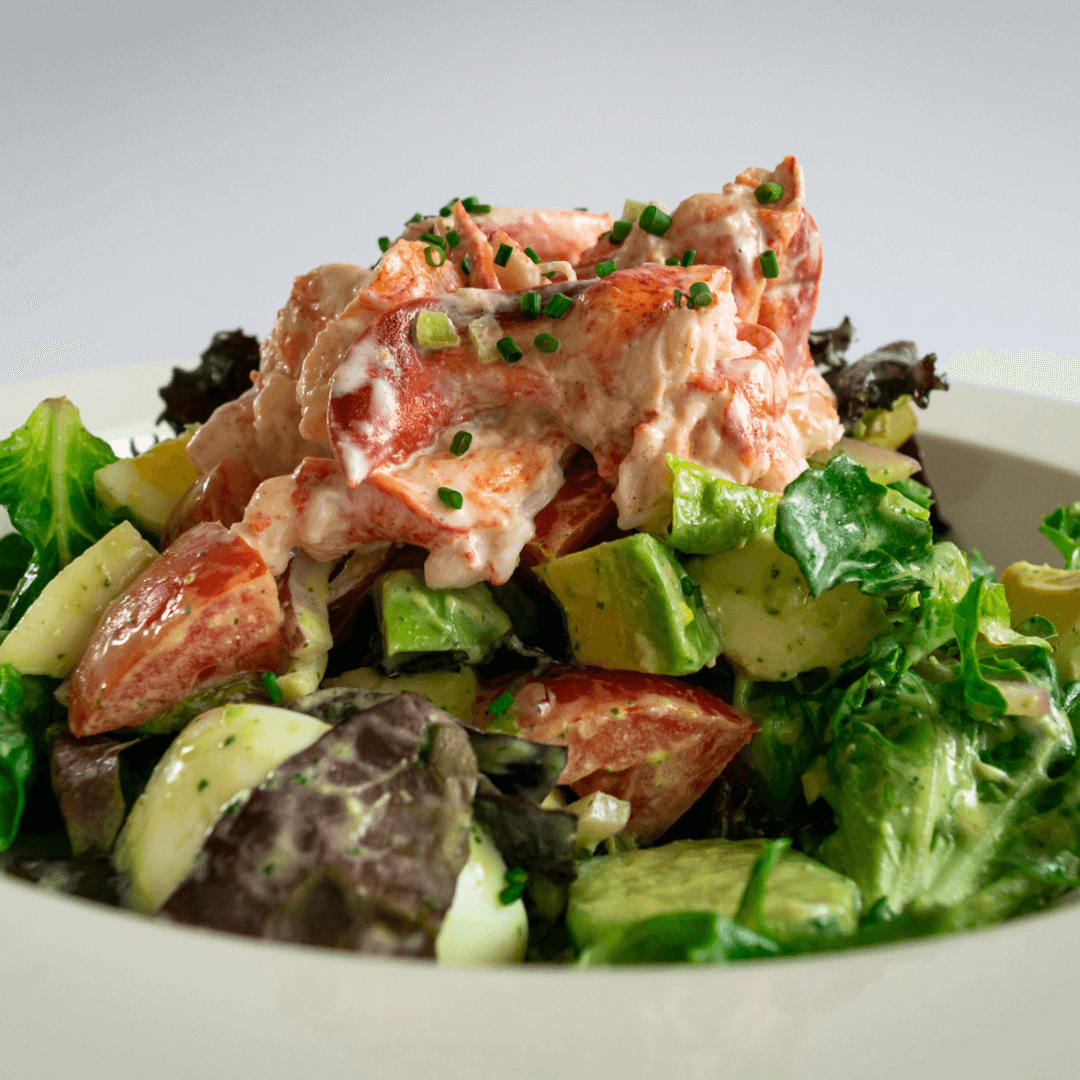 Lobster cobb salad with mixed greens, avocado, and tomatoes served on a white plate