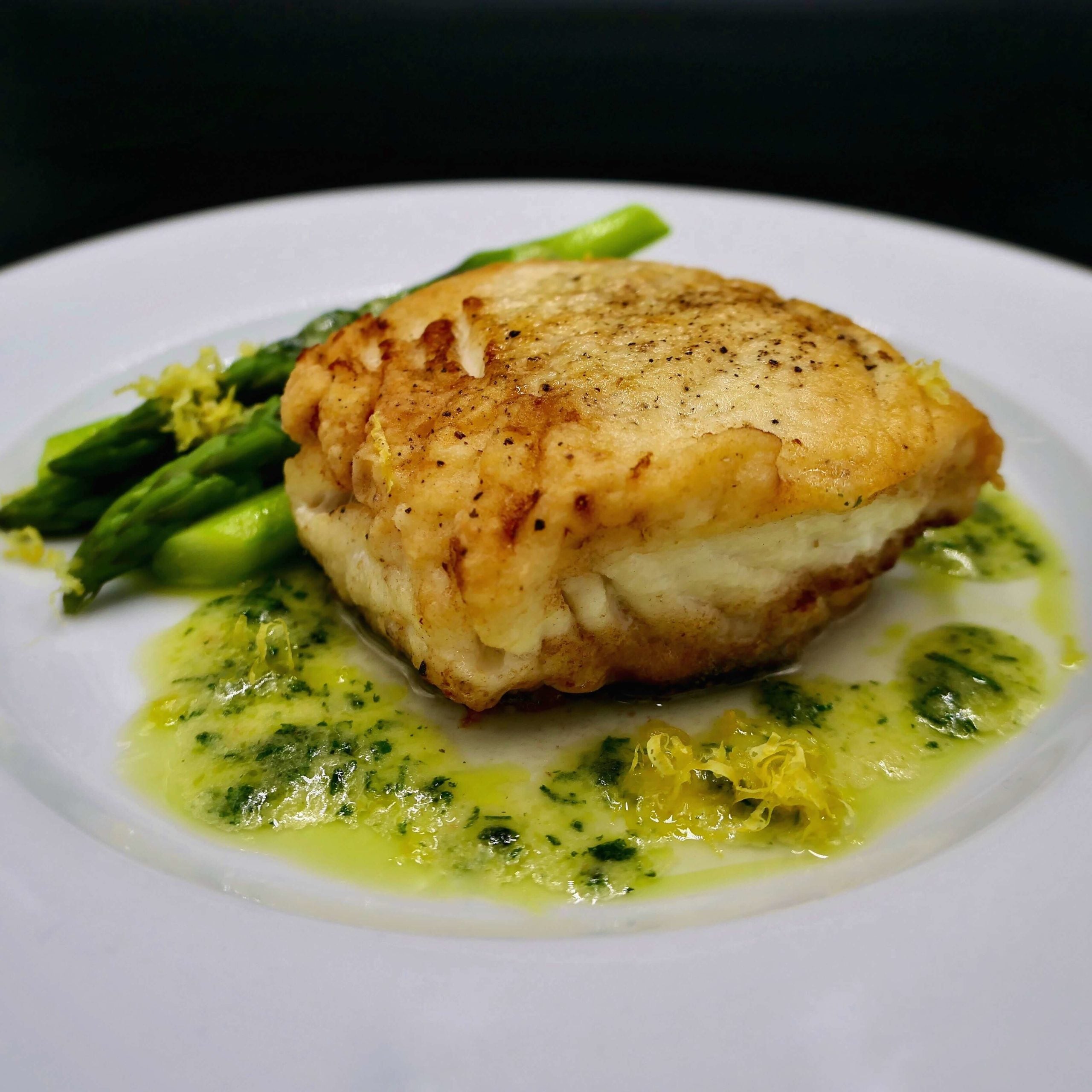 pan fried halibut served with asparagus topped with lemon herb butter sauce on a white plate with black background