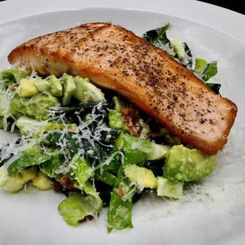 crispy salmon on top of caesar-cobb salad in middle of white plate