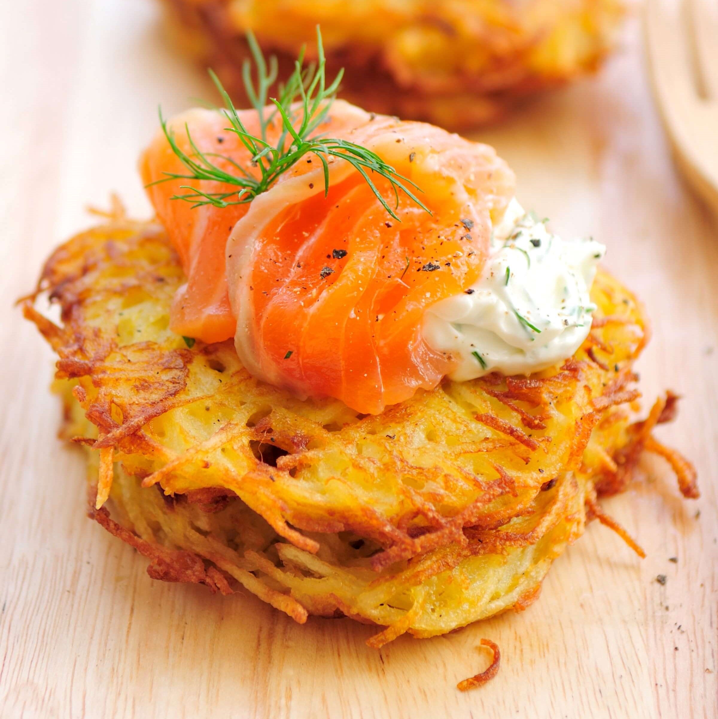 2 crispy potato latkes topped with a dollop of sour cream, smoked salmon and a sprig of dill on a table top