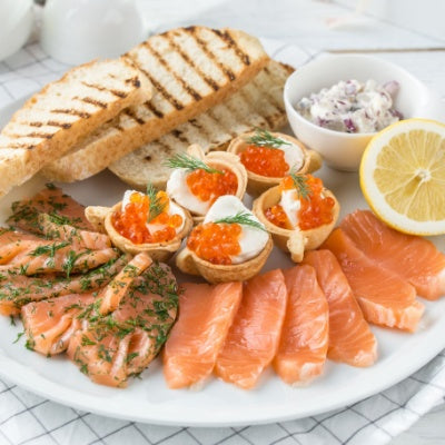 A fish plate with different types of smoked and salted fish, lemon, and toasted bread.