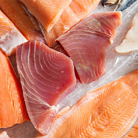 Top-down view of fresh tuna and salmon steaks at a fish market.