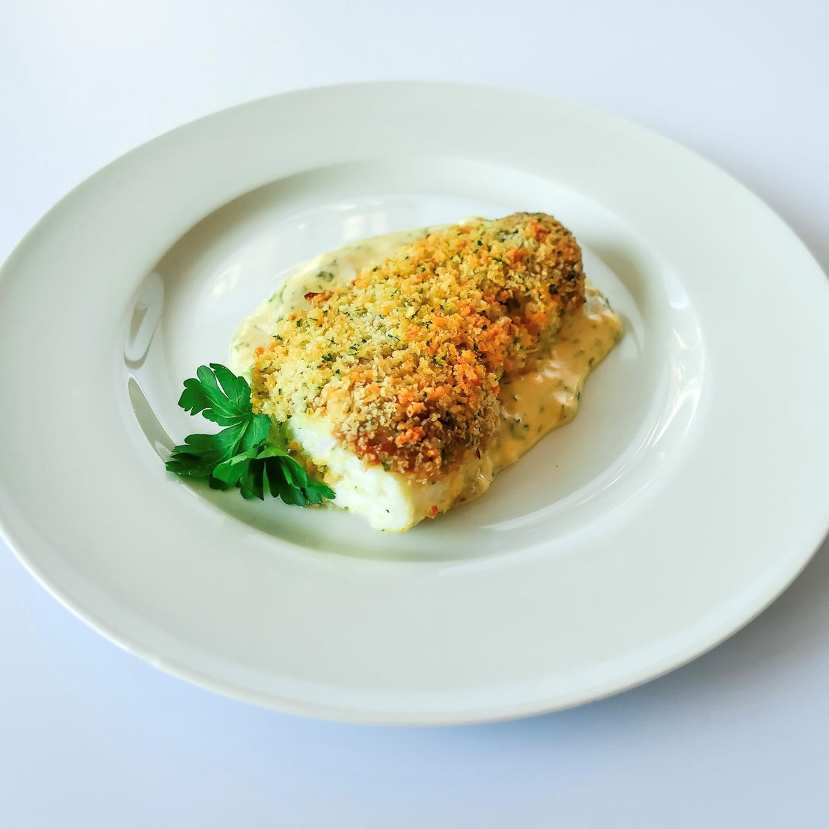 baked breaded haddock served over sauce on a white plate