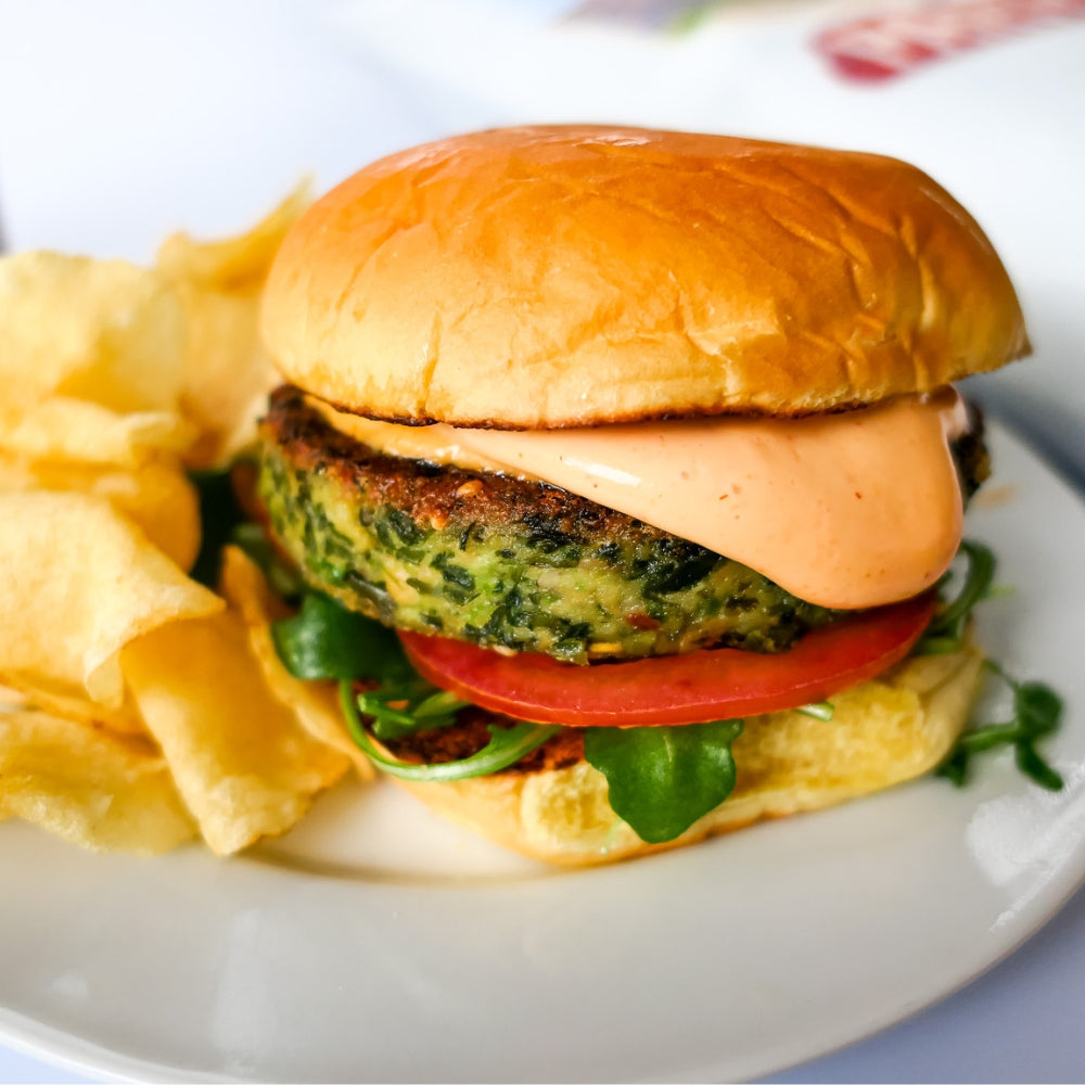 cooked kelp burger on a bun with tomato arugula and spicy aioli, served on a plate with chips