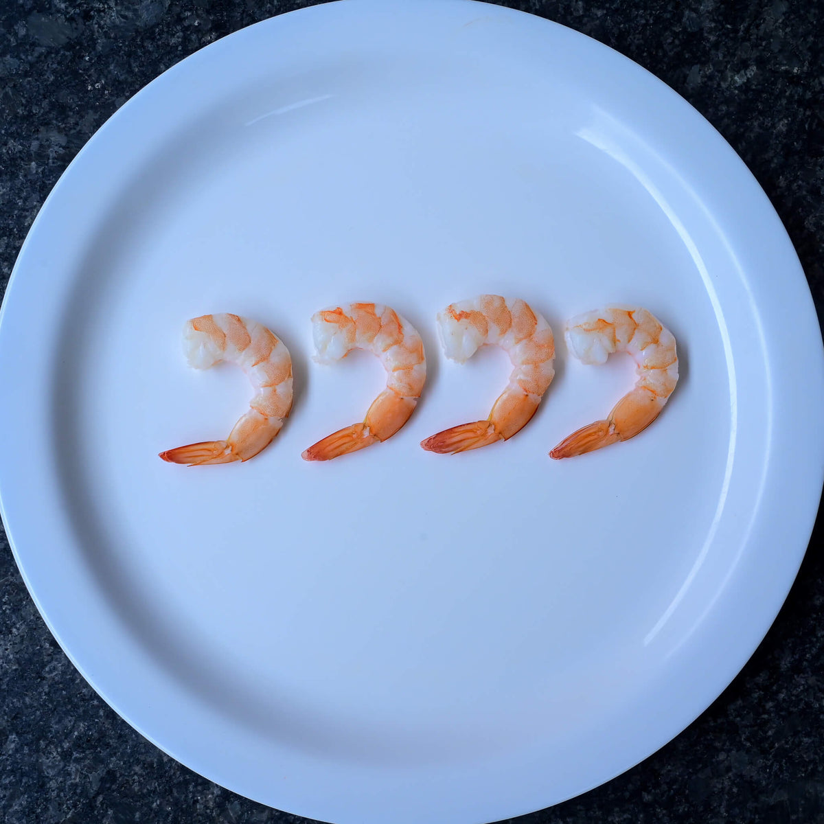 four cooked naked shrimp on a white plate