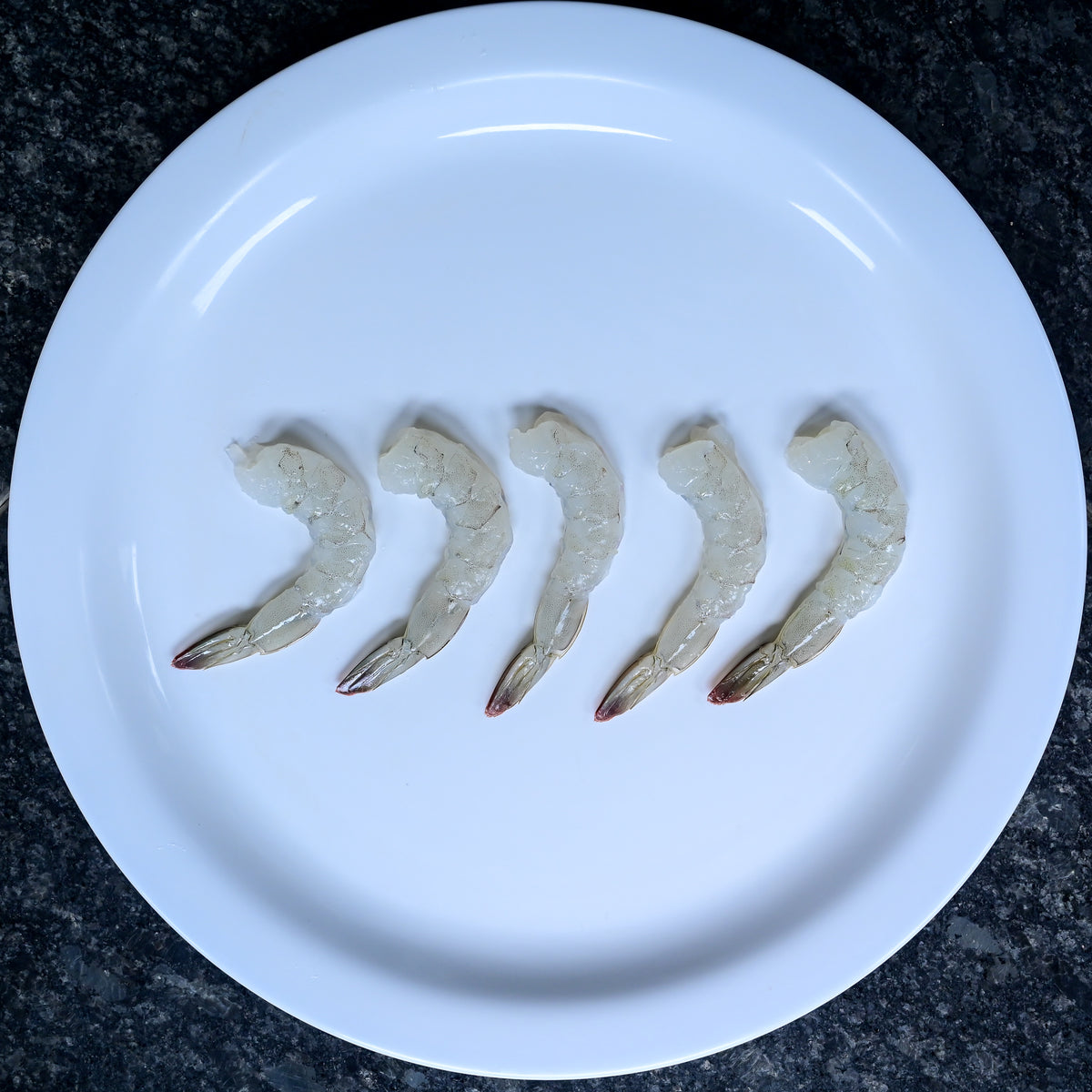 5 raw naked shrimp on a white plate
