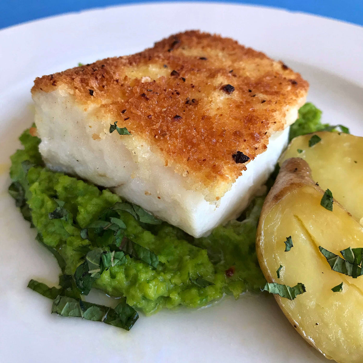 pan fried breaded cod with peas and potatoes on a white plate