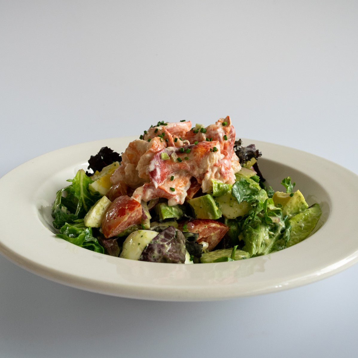 cobb salad topped with lobster meat served in a white bowl