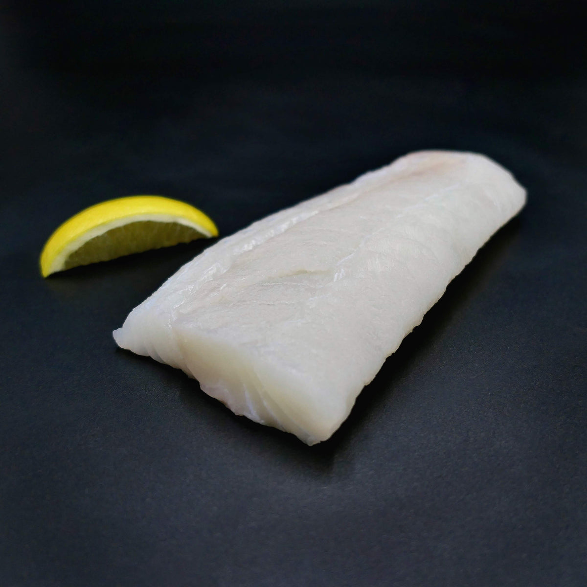 fresh haddock portion on a black background with a lemon wedge