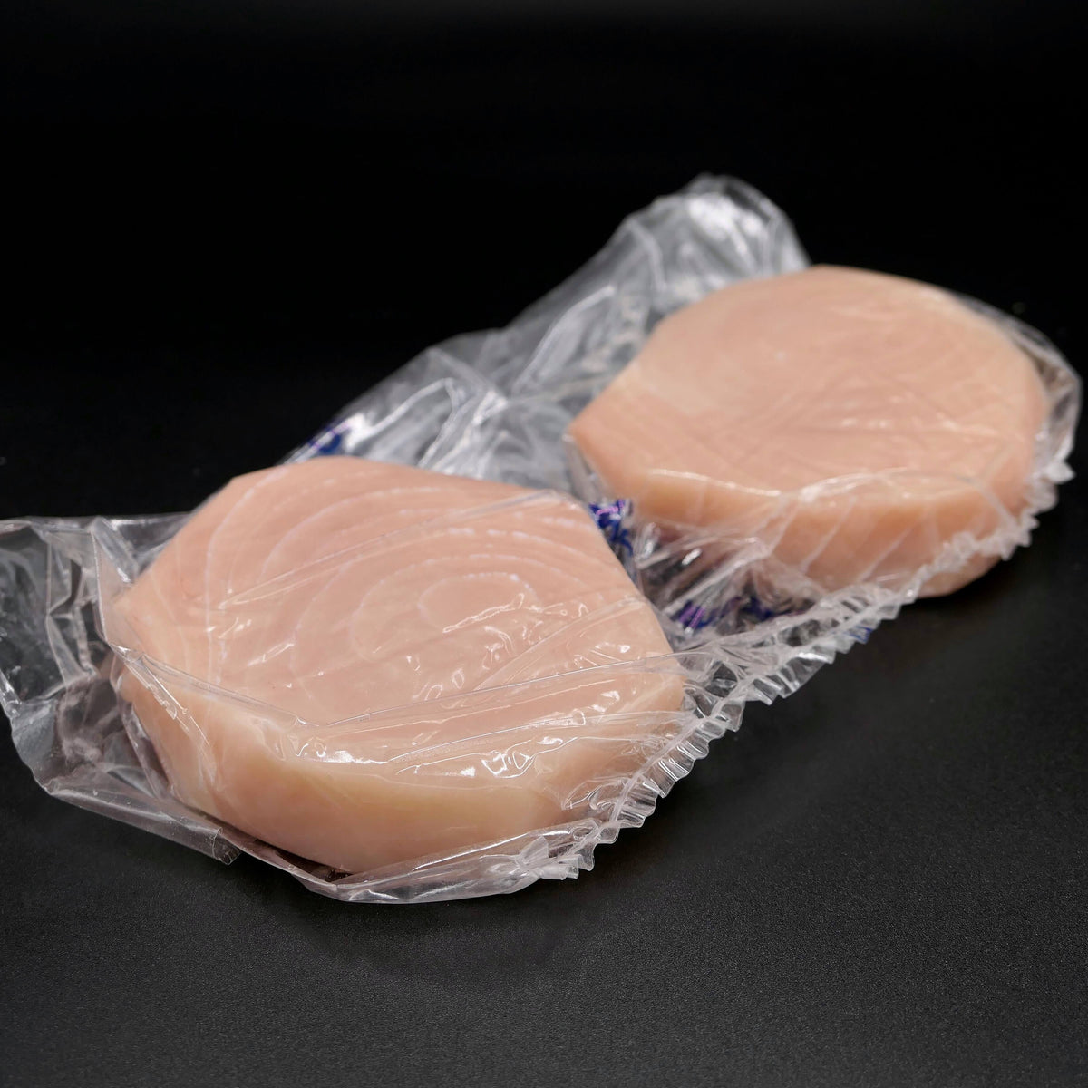 two fresh swordfish steaks in plastic packaging on a black background