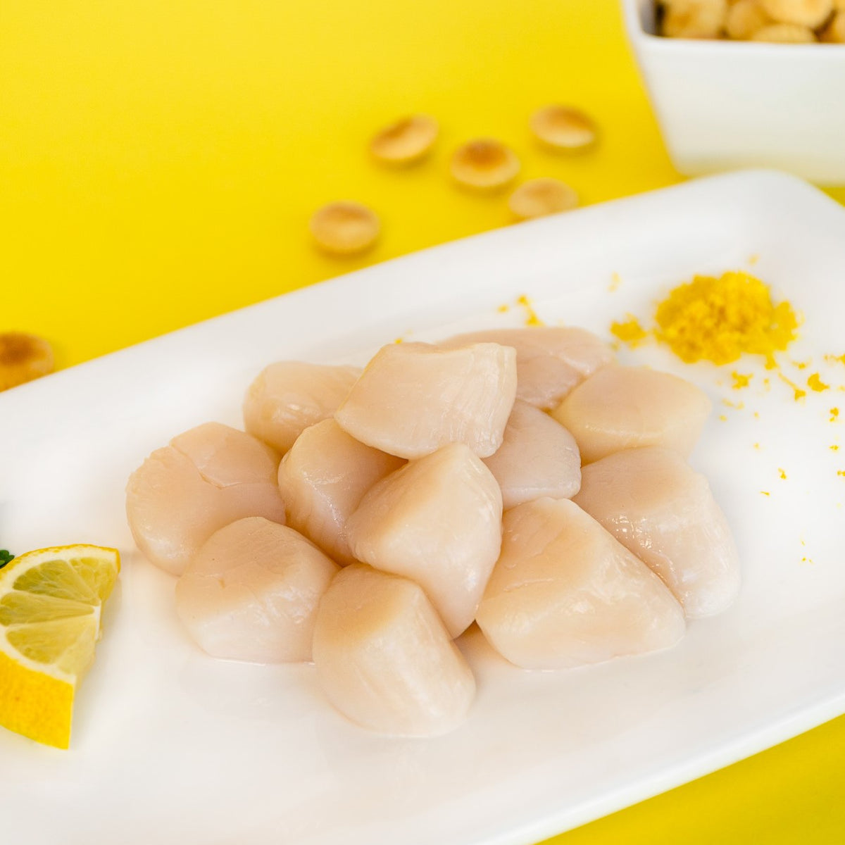 fresh raw sea scallops on a white plate with lemon and parsley on the side