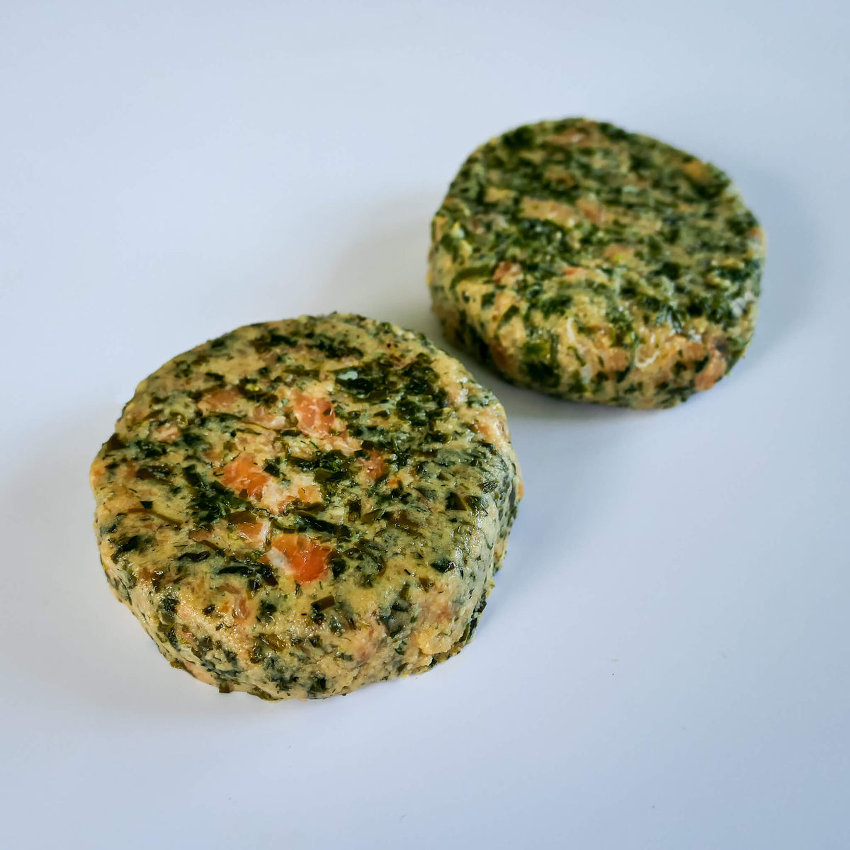 Two raw salmon kelp burgers on a white background