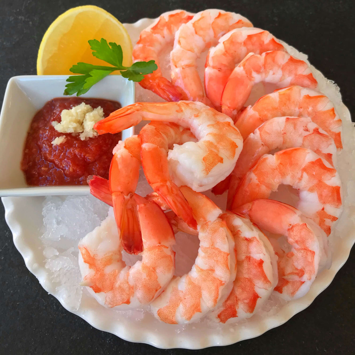 serving plate of cooked shrimp cocktail with cocktail sauce and horseradish with lemon and parsley on the side